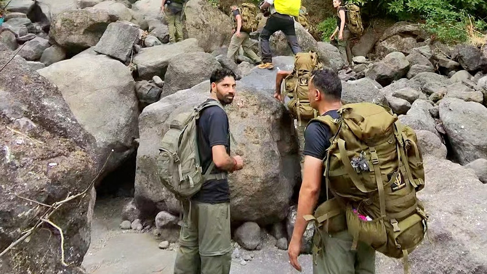 Trekkers with heavy packs scrambling over boulders on a misty forest trail