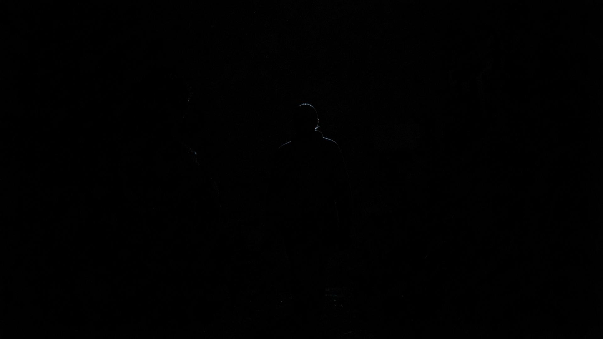 A figure in near-total darkness