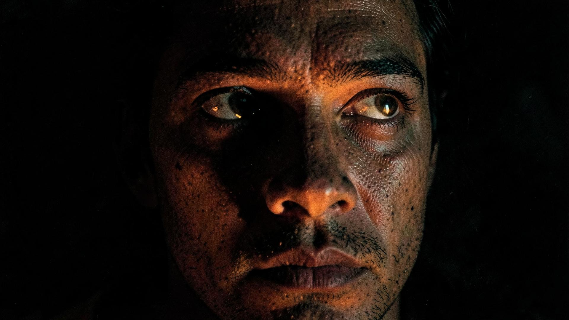 A weathered human face lit by firelight