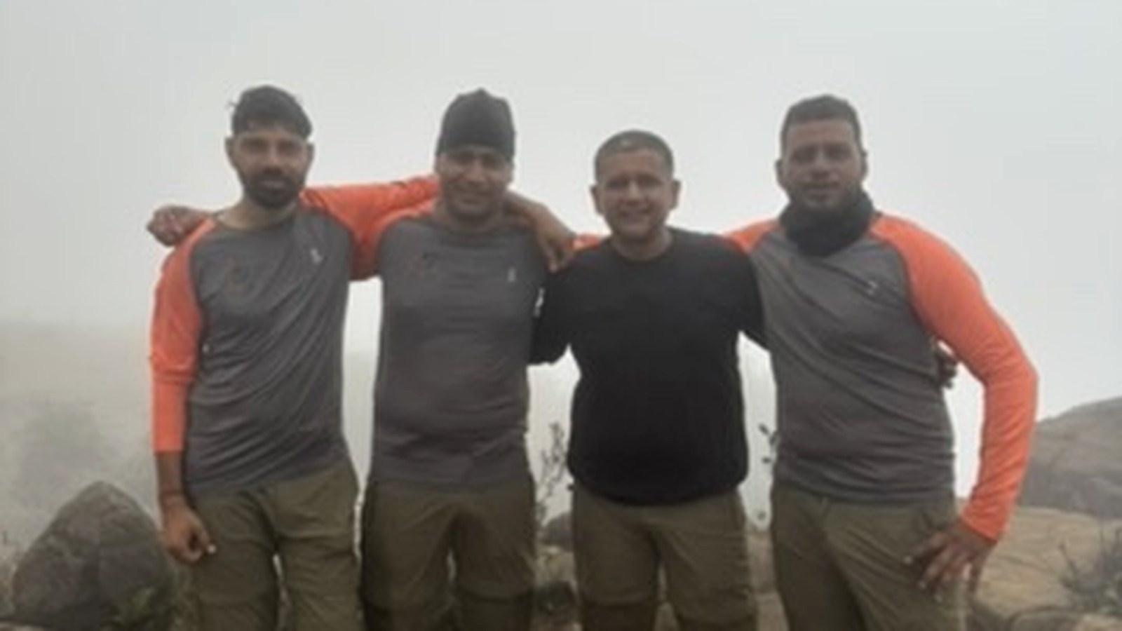 Four expedition leaders standing arm in arm on a mist-covered summit